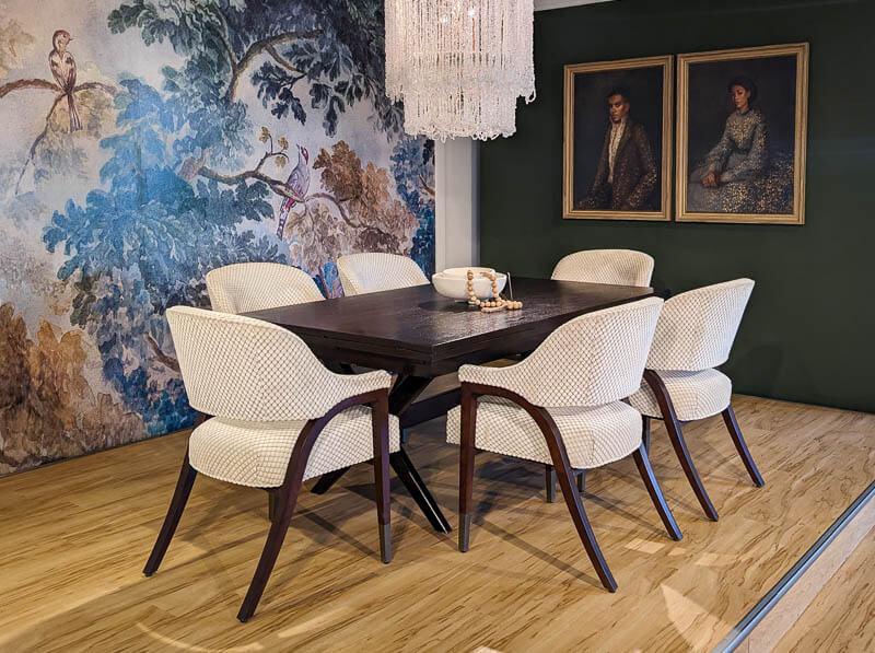 A dining table and chairs under a chandelier with floral wall paper and oil paintings